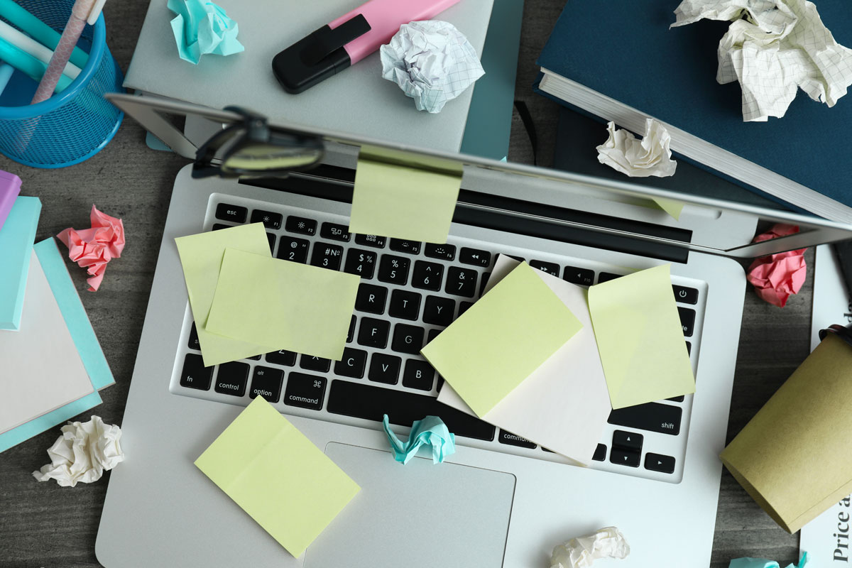 Cluttered workspace with a laptop and scattered notes, representing operational friction and disorganized content workflows.